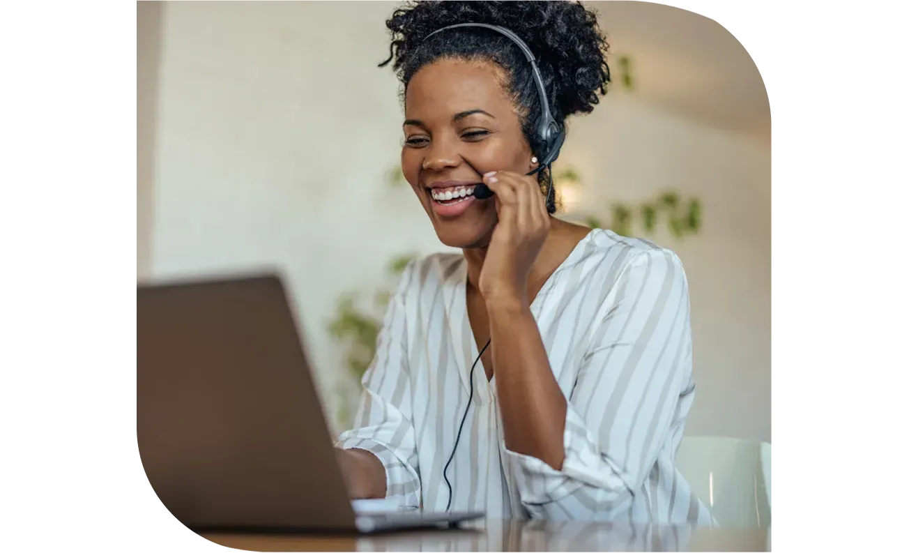 Smiling woman wearing a headset and looking at a laptop.