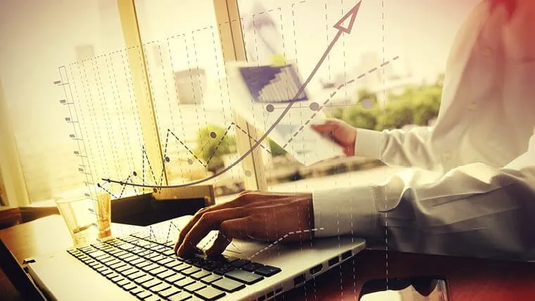 Business professional analyzing financial data on a laptop with overlaid digital charts and graphs.
