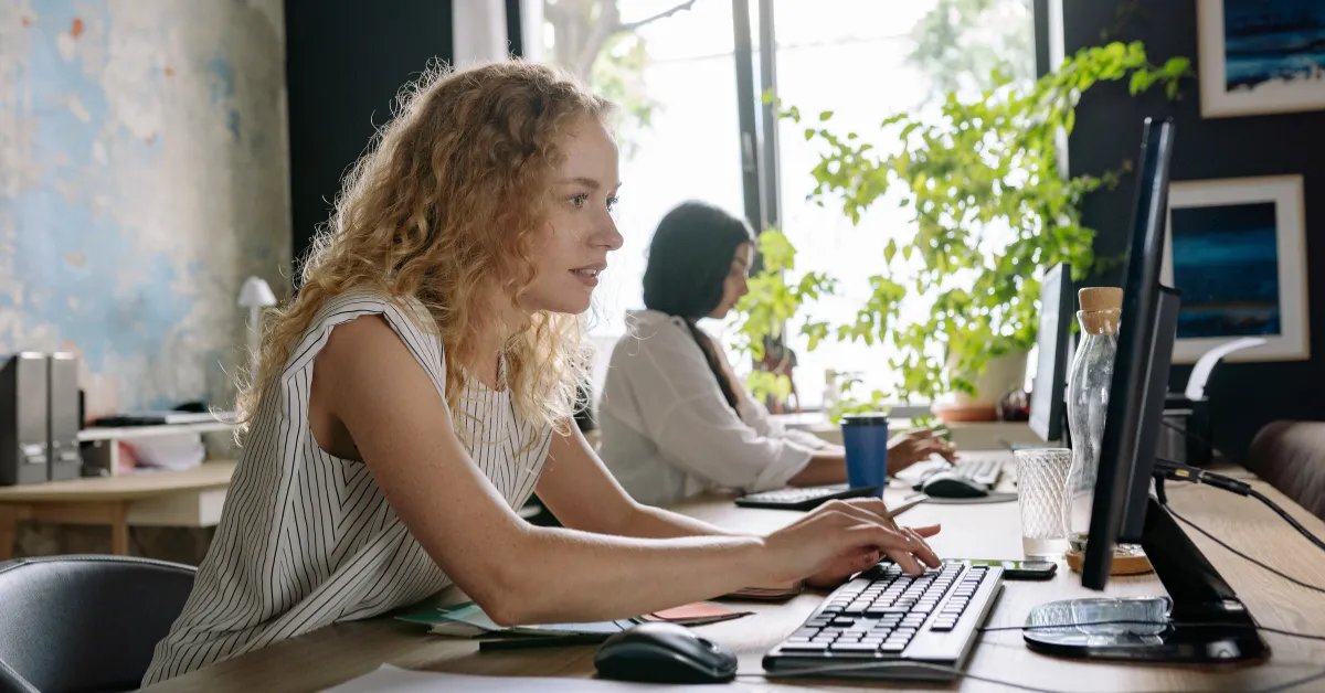 Two coworkers using internal communication tools at their desks in a bright office