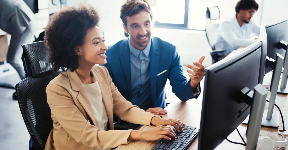 Two colleagues reviewing something together on a desktop monitor in an open office